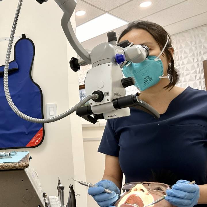 Female endodontist using a dental microscope while starting root canal therapy in the operatory, demonstrating specialized endodontic treatment and what to expect during a root canal procedure.